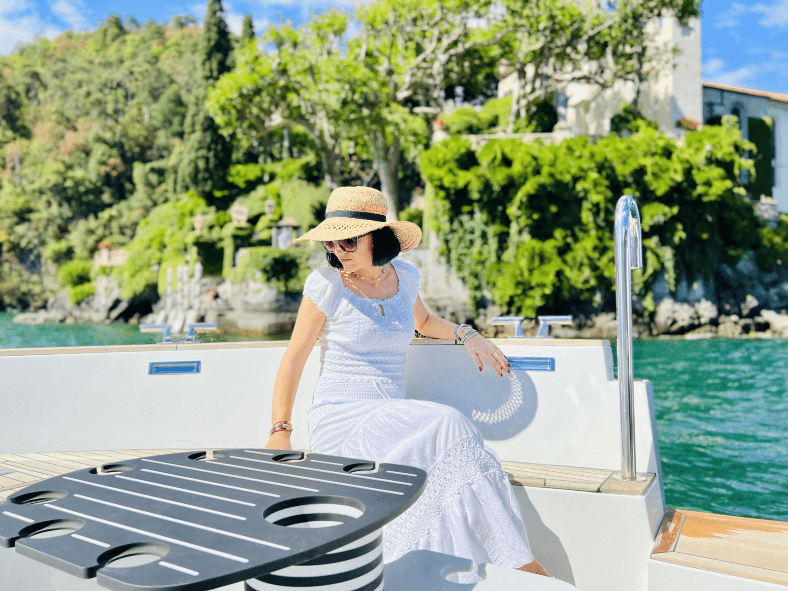 rich woman enjoying boat private cruise in lake como on the best limo tender which is the most luxurious water taxi of lake como with lush vegetation in the back on como holiday