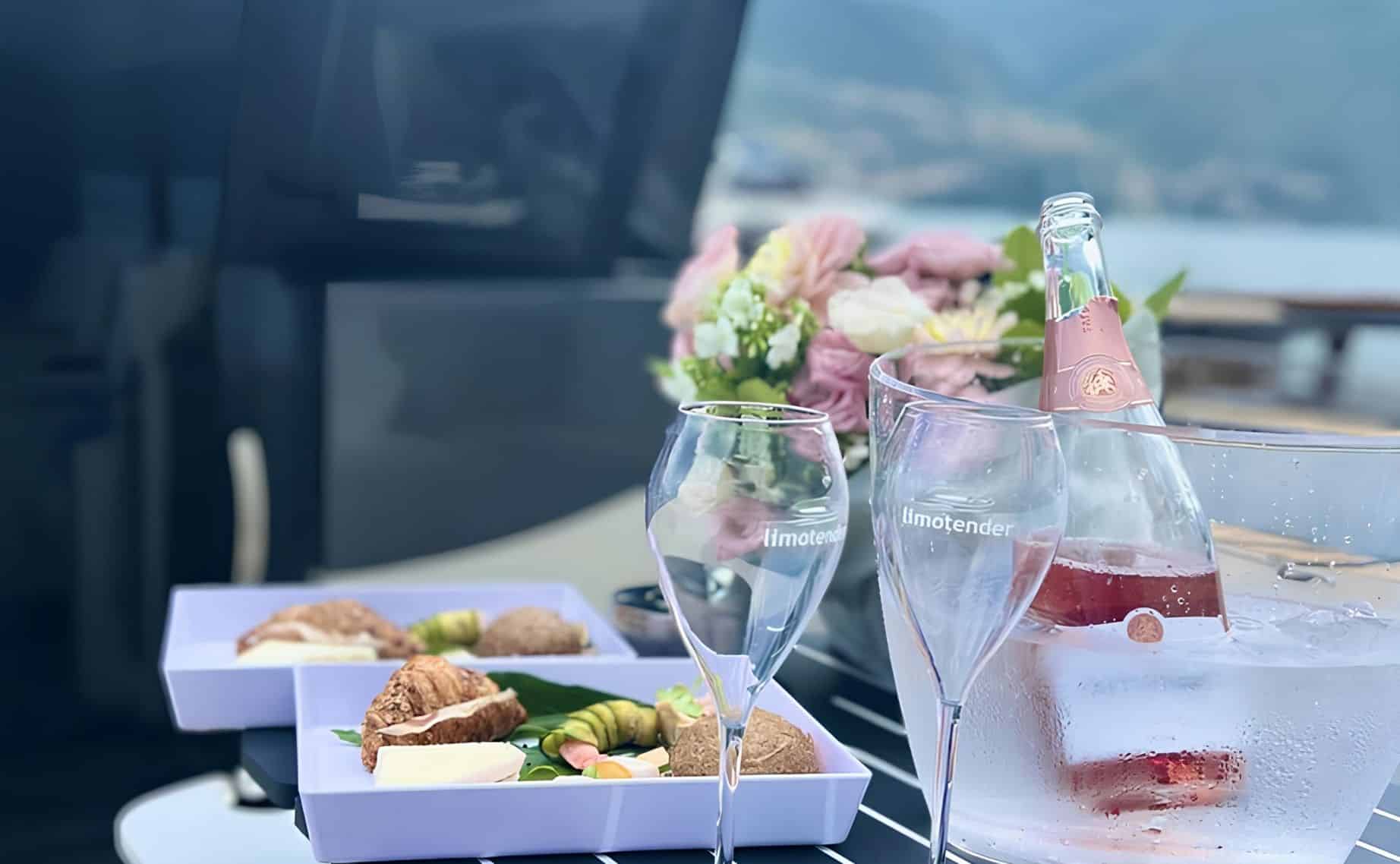 Lunch box color pastello, flute vuoti e bottiglia rosé in glacette su tavolo yacht Limotender sul Lago di Como.