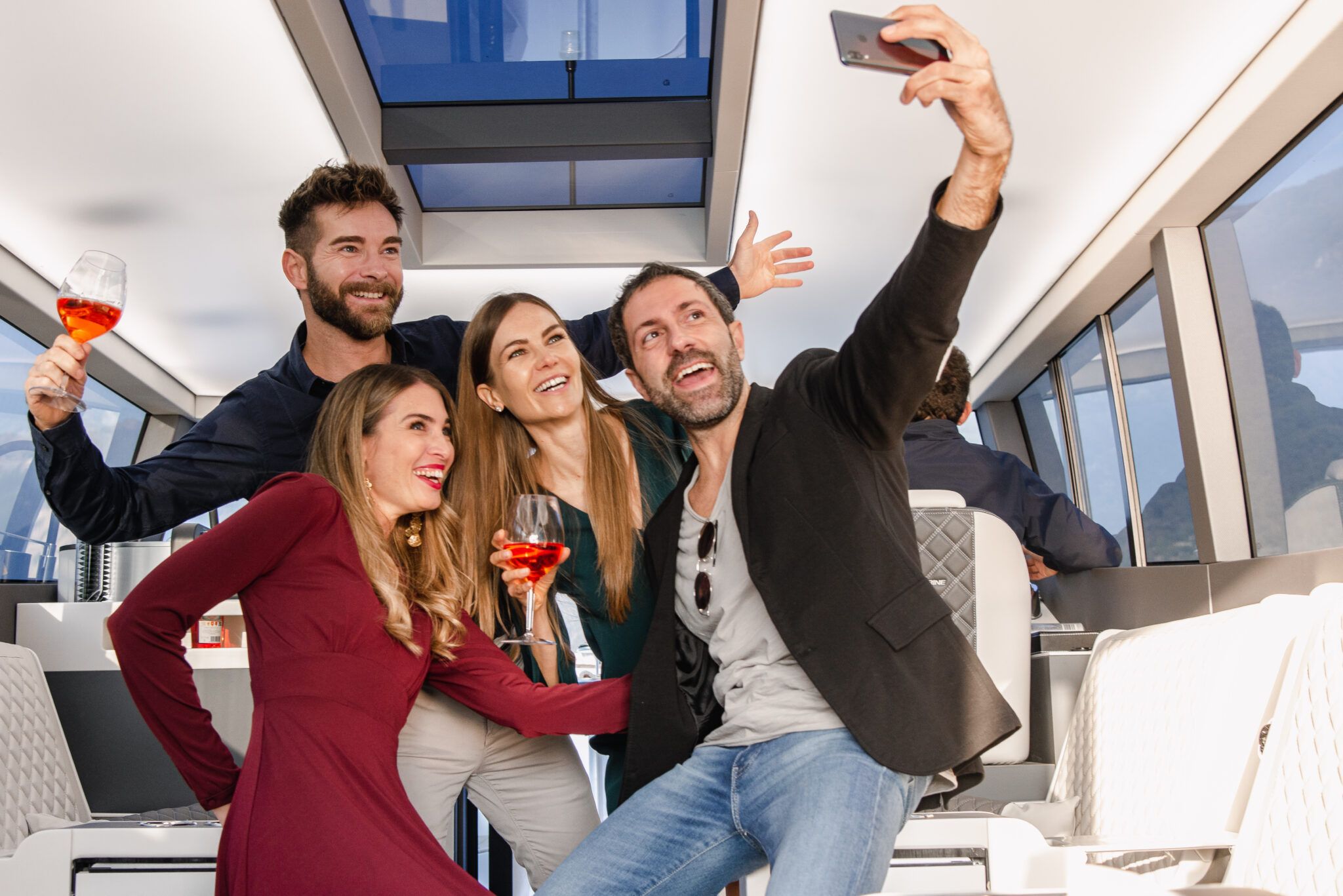 Four stylish people smiling for a selfie with orange cocktails aboard modern Lake Como party boat.
