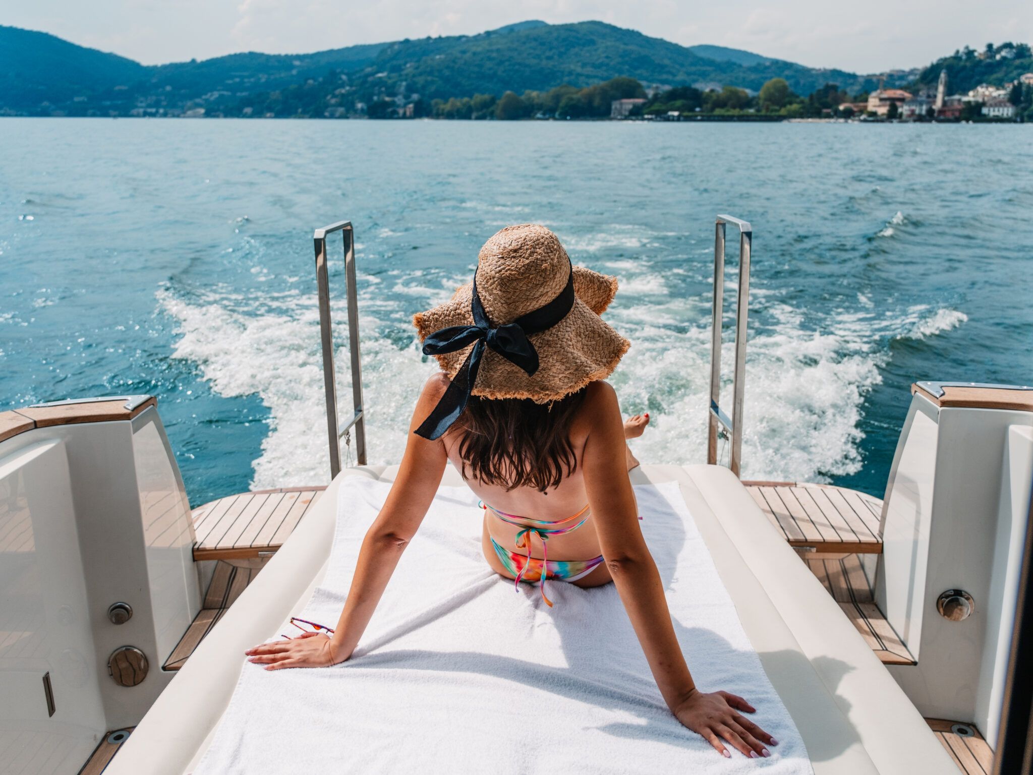 Woman relaxing on yacht sun-pad during Lake Como day cruise, mountains and water wake behind.