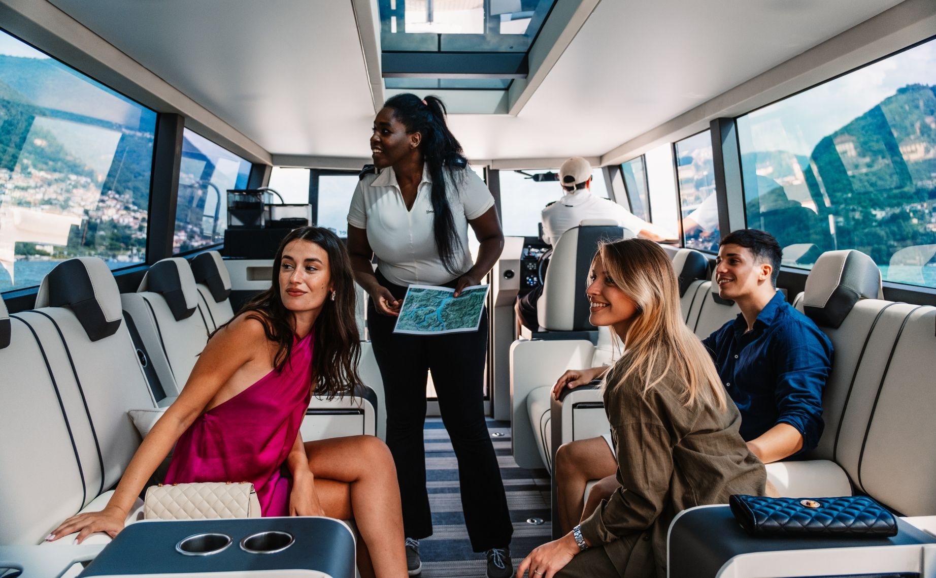 Crew member showing map to diverse group inside panoramic yacht cabin during bespoke Lake Como day tour.